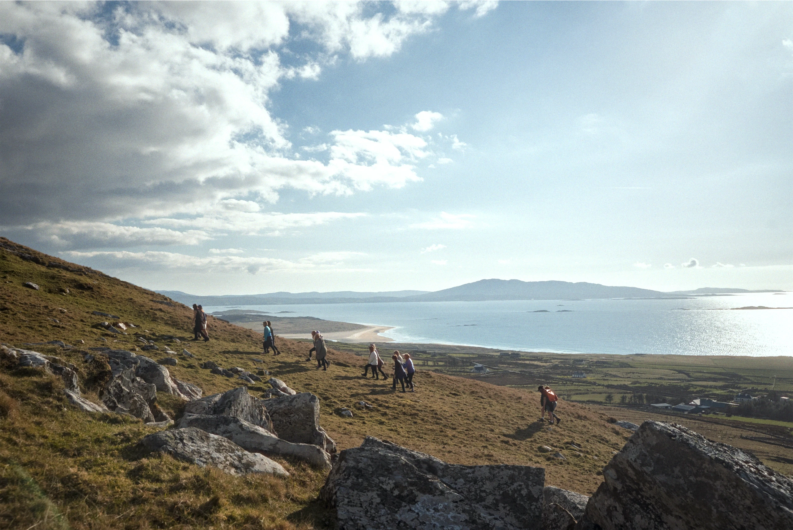 Hikers on a grassy hill overlooking the beach and sea under a cloudy sky in Donegal, Ireland.