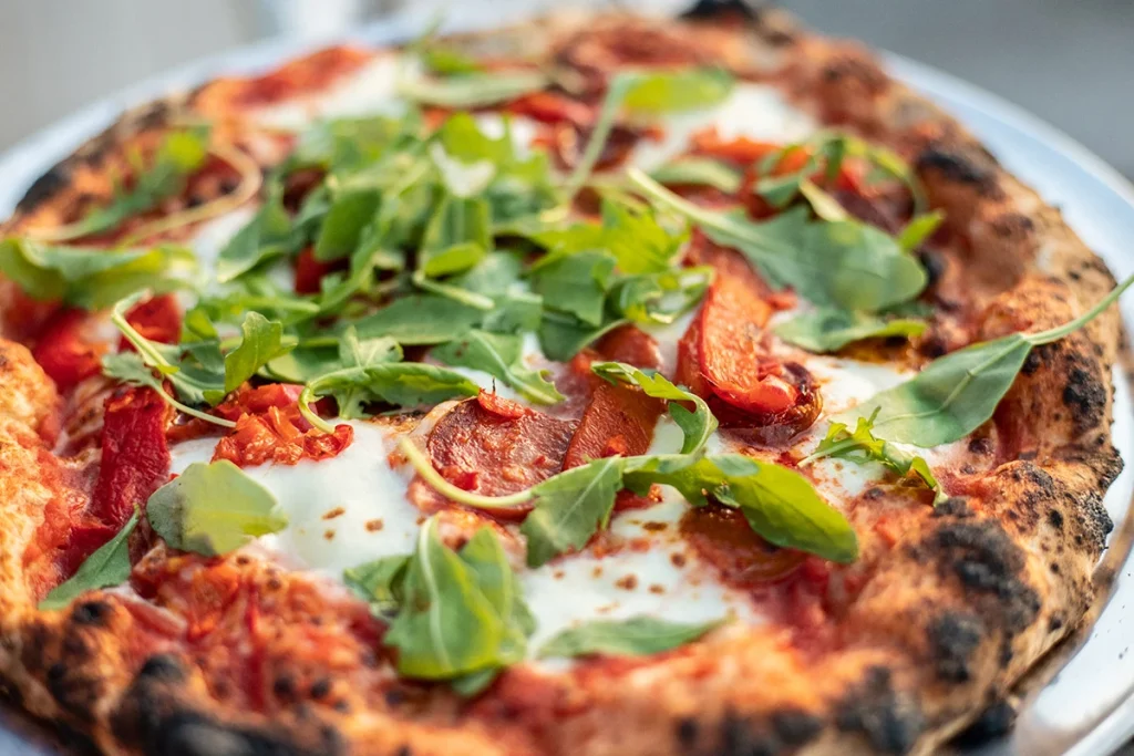 Wood-fired pizza topped with fresh rocket, mozzarella, and roasted red peppers.