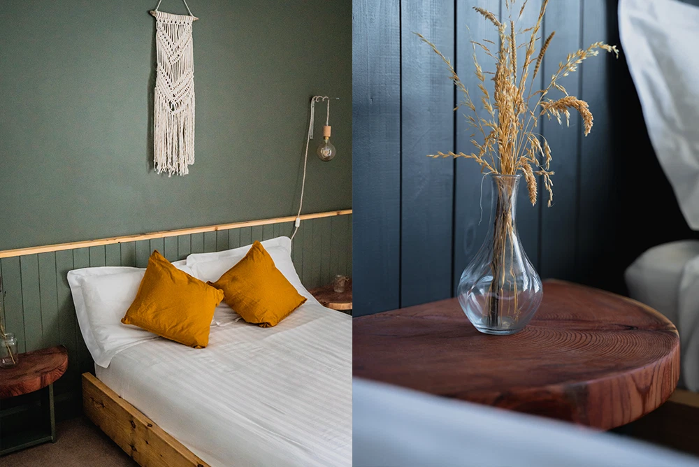 Cosy bedroom with mustard cushions, macramé wall hanging, and rustic bedside table with a vase of dried flowers.