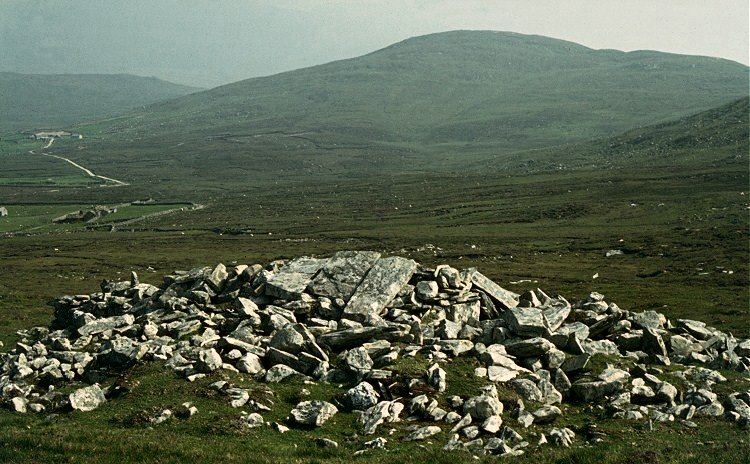 Ancient stone cairn on An Sliabh Liag landscape, Ireland; rolling green hills in the background.