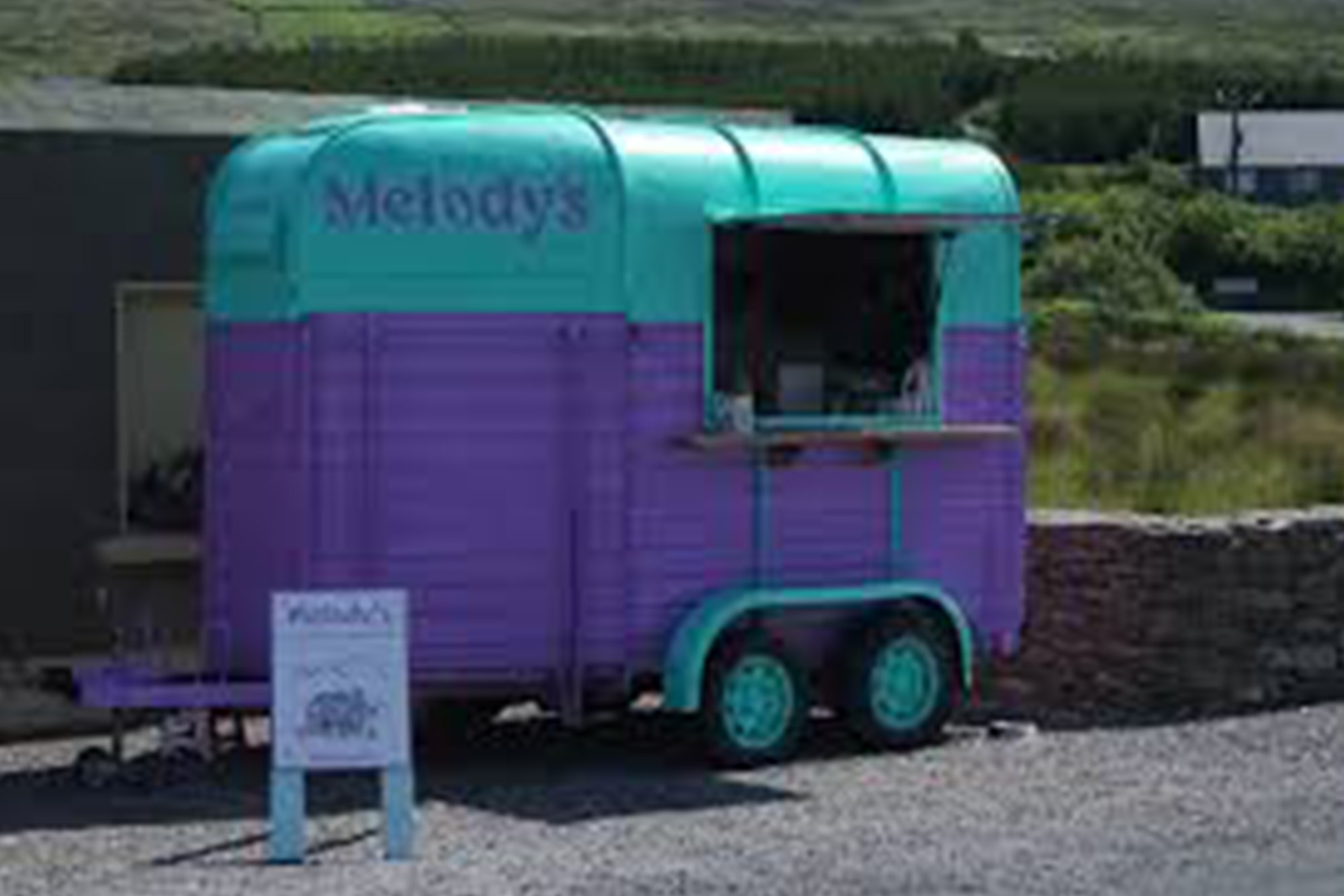 Colourful mobile food van serving refreshments in scenic countryside setting.