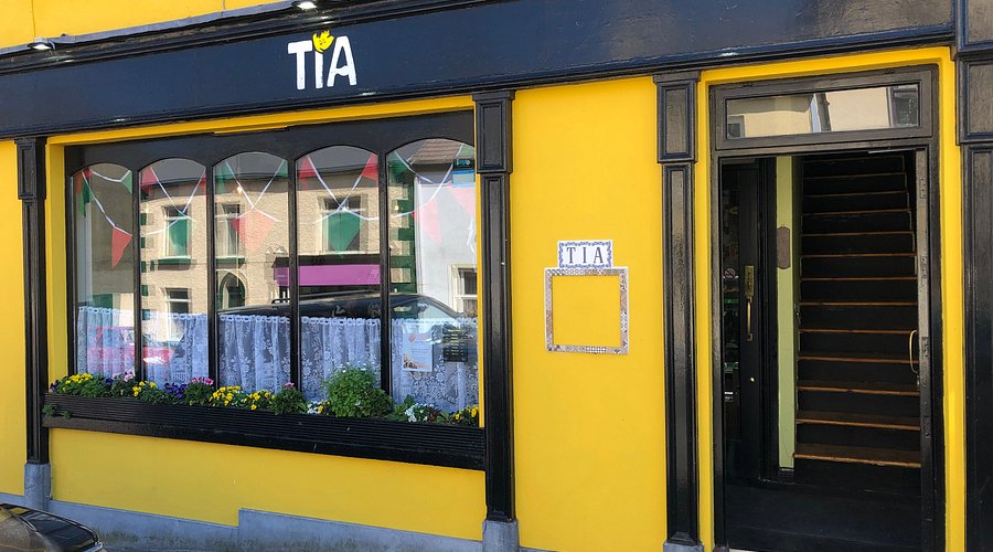 Front of Tia restaurant with yellow facade, window display, and entrance stairs in an Irish town.